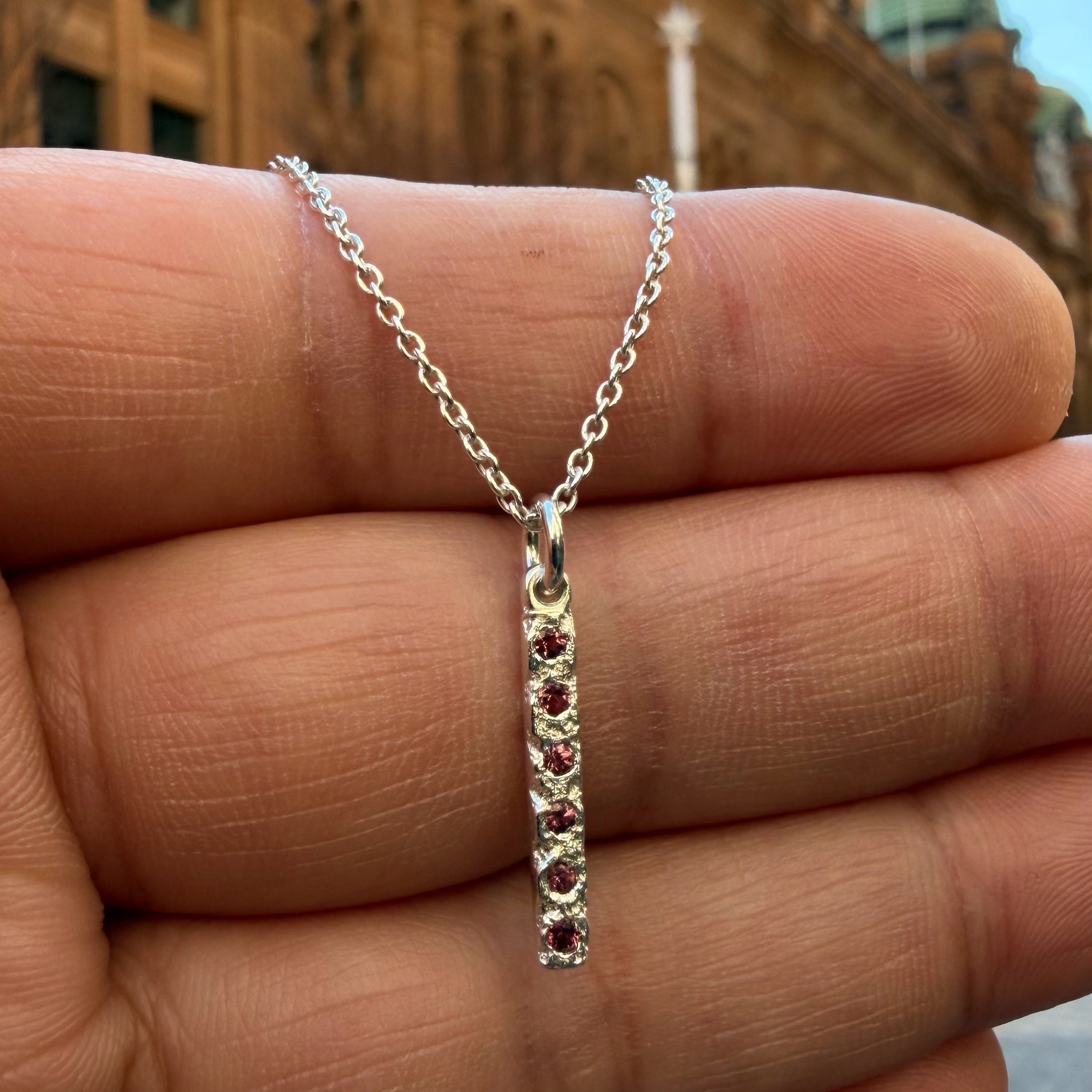 A Sterling silver chain necklace with a small textured rectangle bar pendant with 6 tourmaline birthstones on the hand for scale