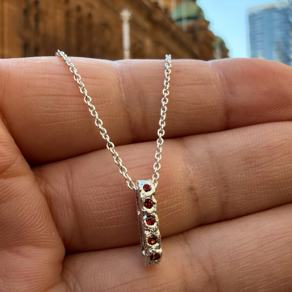 A Sterling silver chain necklace with a small textured oval bead pendant with 12 garnet birthstones, 5 on the front going all the way around, on the hand for scale