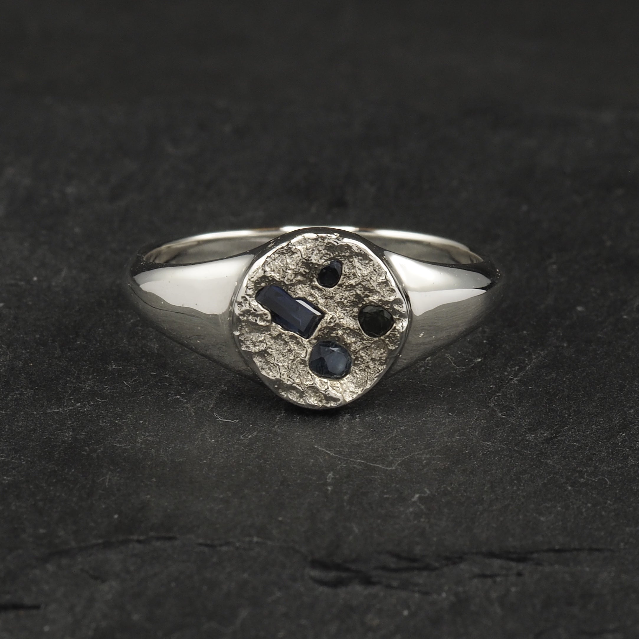 Small textured round signet ring with a terrain texture that signifies the land from high able, with four cast in place Australian blue sapphires