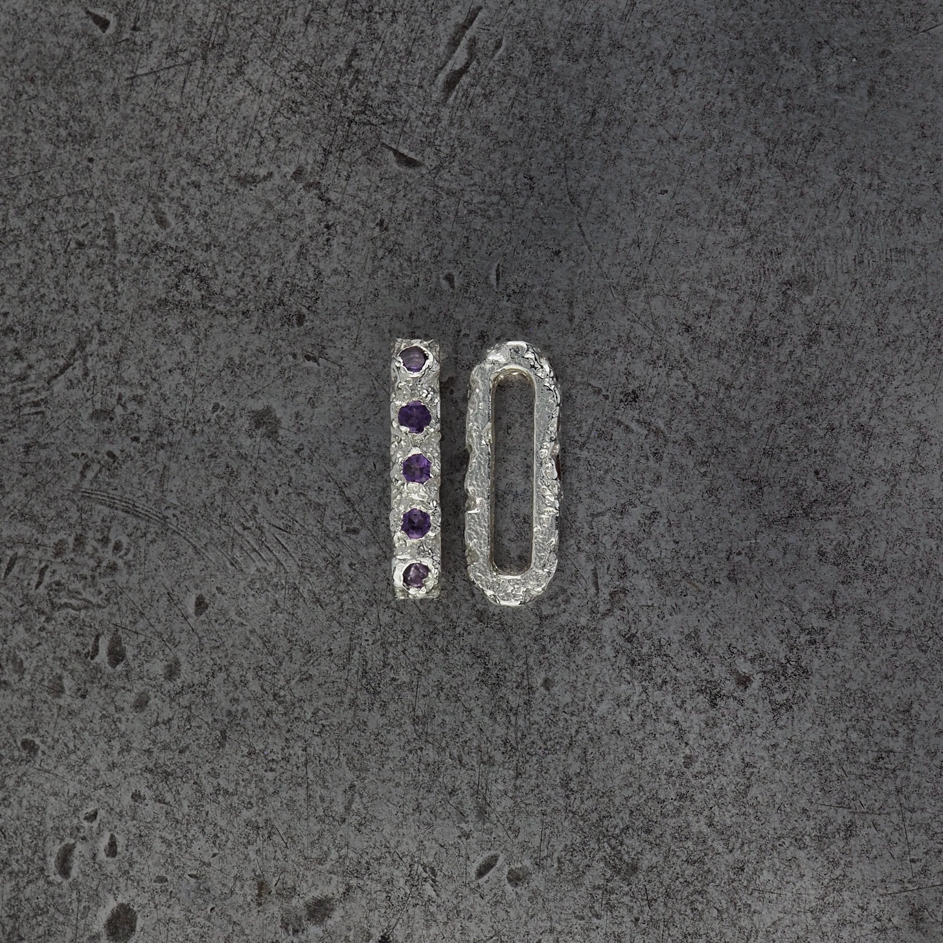 Two small textured oval bead pendants, one with amethyst birthstones and the other showing the side profile on a steel textured background.