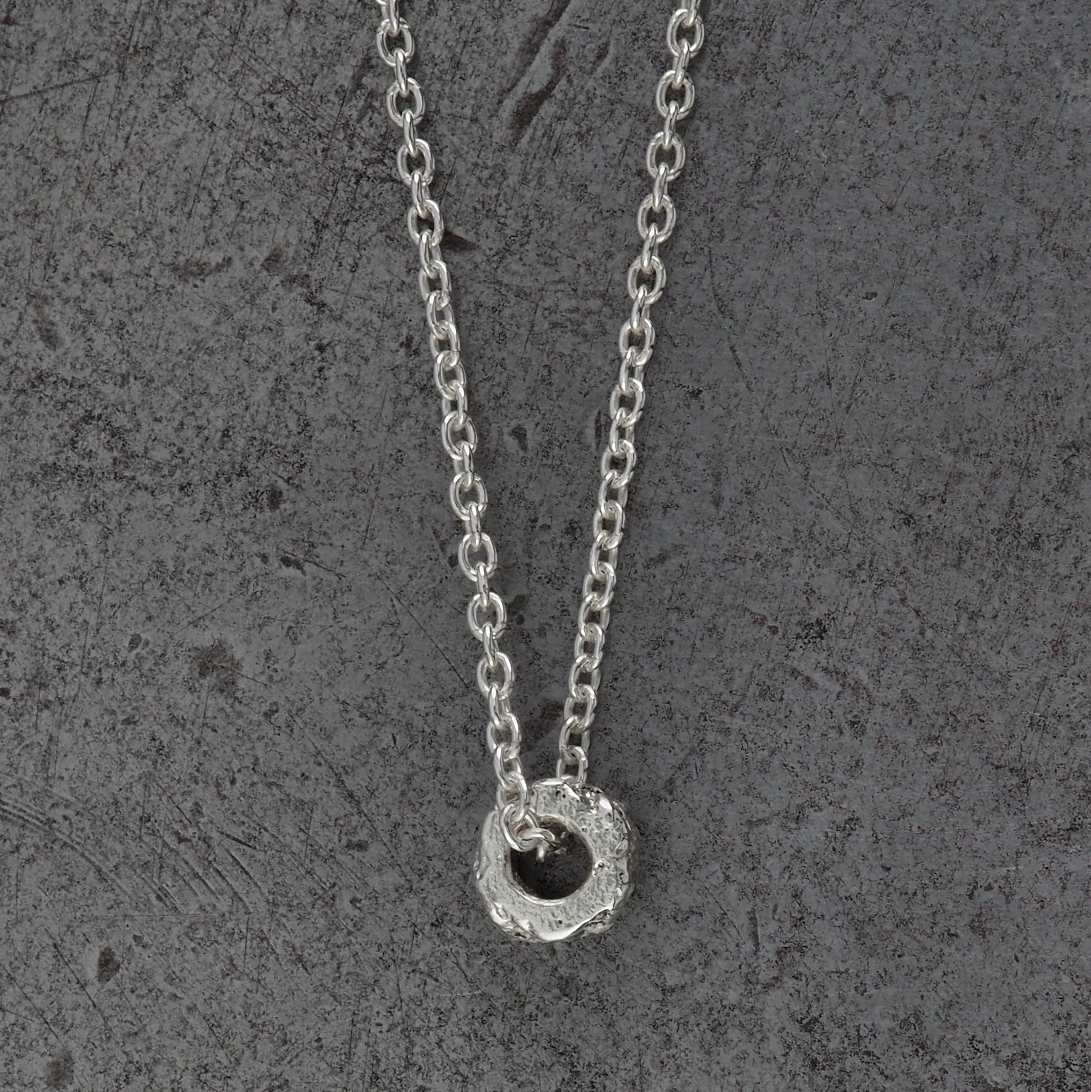 A Sterling silver chain necklace with a small textured cylindrical bead pendant with aquamarine birthstones, side profile displayed on a steel background.